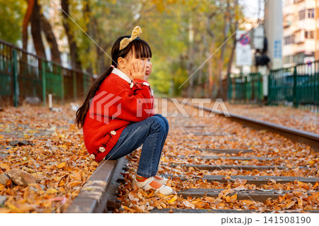 Little girl wearing a red sweater crouches on an old railway track ,On an autumn day 141508190