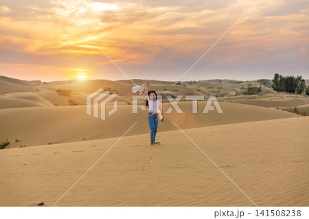 Back view of a little girl walking on a sand dune toward the bright sunset. 141508238