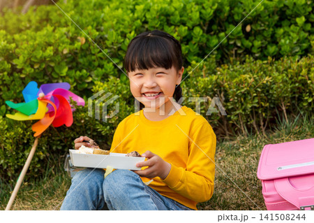 Asian little girl eating meal outdoors in park with colorful pinwheel, happy childhood and leisure lifestyle concept Asian little girl eating meal outdoors in park with colorful pinwheel, happy childhood and leisure lifestyle concept 141508244