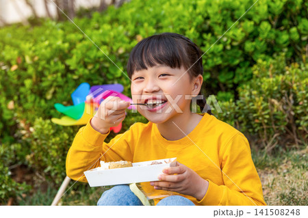 Asian little girl eating meal outdoors in park with colorful pinwheel, happy childhood and leisure lifestyle concept Asian little girl eating meal outdoors in park with colorful pinwheel, happy childhood and leisure lifestyle concept 141508248