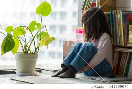 Lonely Little Asian Girl Sitting by Window Thinking and Looking Out Lonely Little Asian Girl Sitting by Window Thinking and Looking Out 141509074
