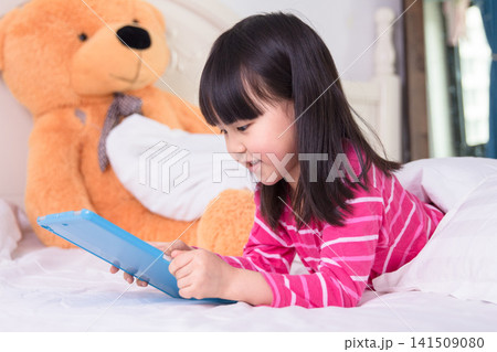 Happy Asian Child Girl Watching Cartoons on Tablet in Bed at Night Happy Asian Child Girl Watching Cartoons on Tablet in Bed at Night 141509080