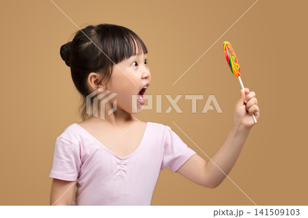 Surprised Asian Little Girl Reaching for Rainbow Lollipop Held by Adult Hand Surprised Asian Little Girl Reaching for Rainbow Lollipop Held by Adult Hand 141509103
