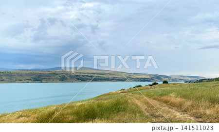 Tbilisi Sea reservoir stretches beside open grassland and a rural shoreline under layered clouds, supporting travel promotion Tbilisi Sea reservoir stretches beside open grassland and a rural shoreline under layered clouds, supporting travel promotion 141511023