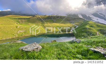 Green Abudelauri Lake collects mountain runoff beneath cloud-covered ridges in Georgia, illustrating alpine hydrology Green Abudelauri Lake collects mountain runoff beneath cloud-covered ridges in Georgia, illustrating alpine hydrology 141511052