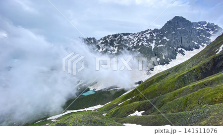 Clouds reveal White Abudelauri Lake below Chaukhi Pass in Georgia, where turquoise glacial water, snowfields and steep slopes Clouds reveal White Abudelauri Lake below Chaukhi Pass in Georgia, where turquoise glacial water, snowfields and steep slopes 141511076