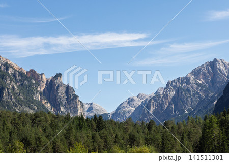 Rugged Dolomite Peaks Framing a Forested Mountain Gap Under Blue Sky in Italy Rugged Dolomite Peaks Framing a Forested Mountain Gap Under Blue Sky in Italy 141511301