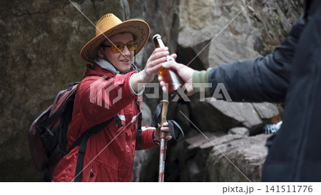 A man passes a bottle of beer to his friend in the mountains. A gay couple is having fun in nature. Travel and tourism 141511776