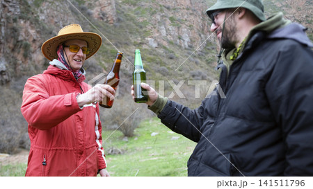 Guys drink beer outdoors. Two gay men are holding bottles of alcoholic beer and smiling at each other. The scene is carefree and friendly Guys drink beer outdoors. Two gay men are holding bottles of alcoholic beer and smiling at each other. The scene is carefree and friendly 141511796