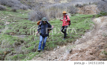 Two gay men are walking in a mountainous area. Weekend camping trip. A group of travelers descends from the mountain along a dirt path 141511856