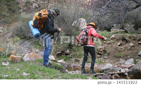 Two travelers cross a small river through a makeshift ferry. Students are walking through the forest in search of adventure 141511922