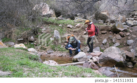 Two people are walking along the riverbank, one of them wearing a cowboy hat. The scene is peaceful and serene 141511931