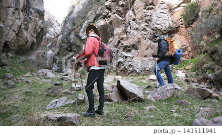 Two men are hiking in a rocky area. A group of tourists walks along the gorge looking around. The travelers are walking along a rocky path Two men are hiking in a rocky area. A group of tourists walks along the gorge looking around. The travelers are walking along a rocky path 141511941