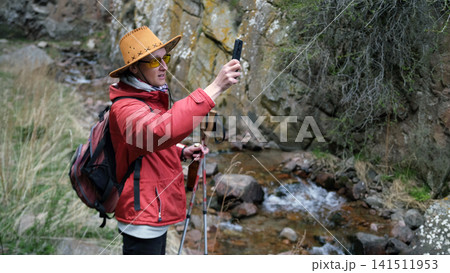 A young guy in a cowboy hat and a red jacket is photographing a river near a rocky mountain. A lone traveler walks through the expanses of the canyon A young guy in a cowboy hat and a red jacket is photographing a river near a rocky mountain. A lone traveler walks through the expanses of the canyon 141511953