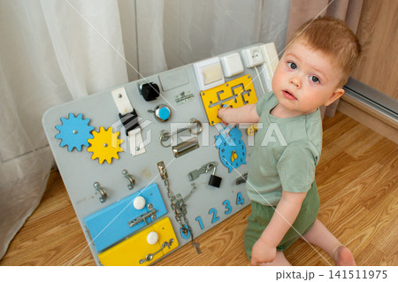 Little boy pressing buttons and turning knobs on busyboard. Exploring world through hands. Montessori style education at home. Fine motor growth in early years Little boy pressing buttons and turning knobs on busyboard. Exploring world through hands. Montessori style education at home. Fine motor growth in early years 141511975
