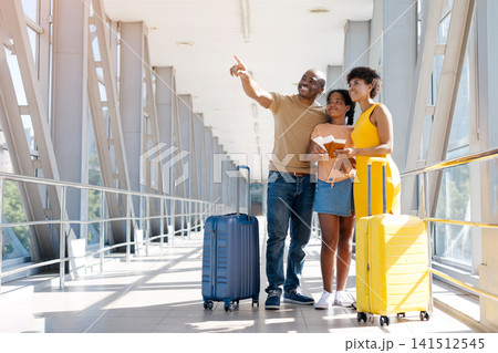 Smiling Black father pointing toward airport signs while standing with her family 141512545