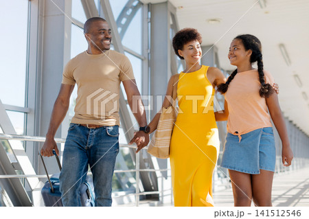 Smiling Black parents walking with their daughter through bright airport terminal Smiling Black parents walking with their daughter through bright airport terminal 141512546