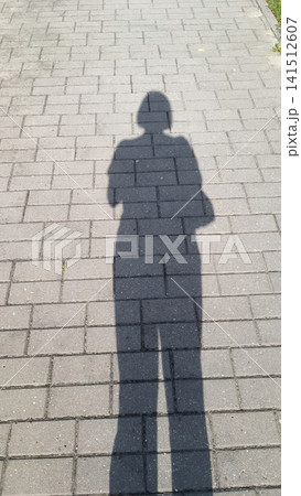 Top down view of a person s elongated shadow cast on a paved surface of rectangular blocks, with the figure holding arms in front. Top down view of a person s elongated shadow cast on a paved surface of rectangular blocks, with the figure holding arms in front. 141512607