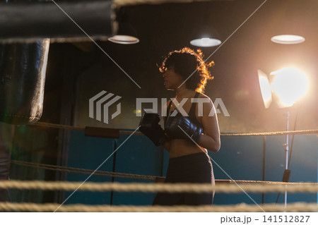 Women self defense girl power. African American woman fighter training punches on boxing ring. Healthy strong girl punching boxing bag. Training day in boxing gym. Strength fit body workout training Women self defense girl power. African American woman fighter training punches on boxing ring. Healthy strong girl punching boxing bag. Training day in boxing gym. Strength fit body workout training 141512827