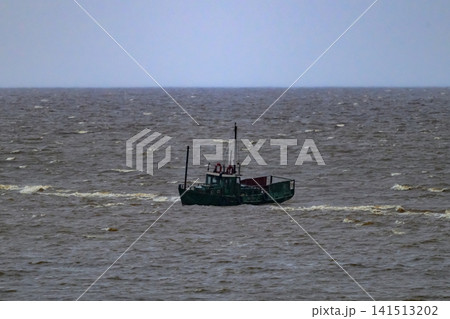 Small fishing boat sails across choppy sea waters. Rough waves crash around the vessel's hull. Sky appears overcast, gray, and distant. No animals or plants visible in this scene Small fishing boat sails across choppy sea waters. Rough waves crash around the vessel's hull. Sky appears overcast, gray, and distant. No animals or plants visible in this scene 141513202