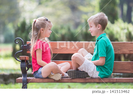 Portrait of two pretty cute children boy and girl having fun time on a bench in summer park outdoors. Portrait of two pretty cute children boy and girl having fun time on a bench in summer park outdoors. 141513462
