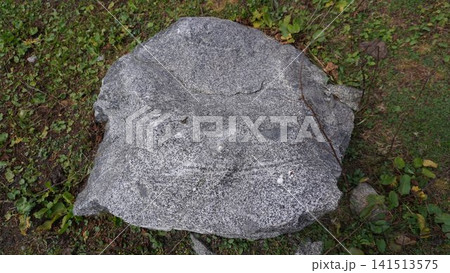 Large gray granite boulder with rough texture sitting on short green grass and soil, stability concept. Large gray granite boulder with rough texture sitting on short green grass and soil, stability concept. 141513575