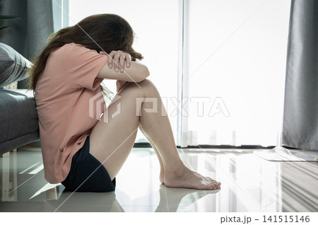 Depressed woman sitting alone in living room caused of sadness or broken heart. Depression is a form of highly negative thinking towards oneself, others and life. Depressed woman sitting alone in living room caused of sadness or broken heart. Depression is a form of highly negative thinking towards oneself, others and life. 141515146