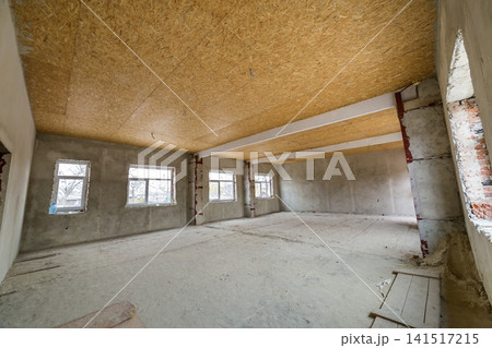 Unfinished apartment or house big loft room under reconstruction. Plywood ceiling, plastered walls, window openings, cement floor. Construction and renovation concept. 141517215