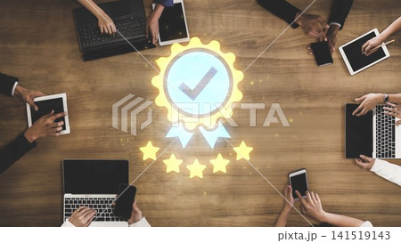Team Collaboration at a Table with Laptops, Tablets, and a Quality Assurance Badge Illuminating from the Center for Business Success Gluon 141519143