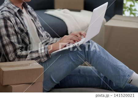 Asian woman using laptop while sitting on floor surrounded by cardboard moving boxes in new apartment Asian woman using laptop while sitting on floor surrounded by cardboard moving boxes in new apartment 141520021