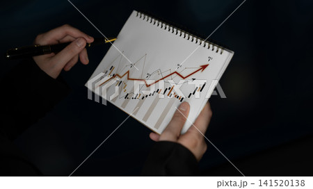 Business person analyzing financial data with a chart on notepad showing upward trends and market growth using a pen in a professional setting Scalp Business person analyzing financial data with a chart on notepad showing upward trends and market growth using a pen in a professional setting Scalp 141520138