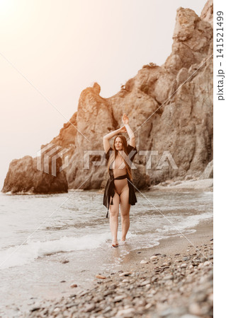 Beach woman fashion walking on a scenic pebbly shore near majestic coastal cliffs during sunset 141521499