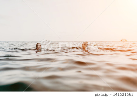Women swimming ocean, two happy friends enjoy refreshing summer sea swim at sunset with copy space 141521563