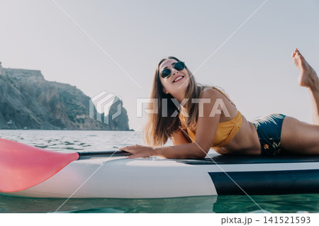 Woman Paddleboard Ocean Relaxing - Smiling woman in a bikini relaxing on a paddleboard in the ocean. Woman Paddleboard Ocean Relaxing - Smiling woman in a bikini relaxing on a paddleboard in the ocean. 141521593