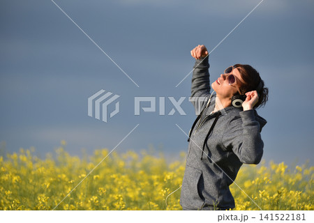Woman with headphones listening to music in a yellow canola flower field Woman with headphones listening to music in a yellow canola flower field 141522181