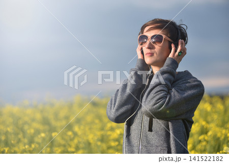 Woman with headphones listening to music in a yellow canola flower field Woman with headphones listening to music in a yellow canola flower field 141522182