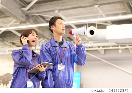 拡声器で案内する女性スタッフとトランシーバーで連絡を取る男性スタッフ 141522572