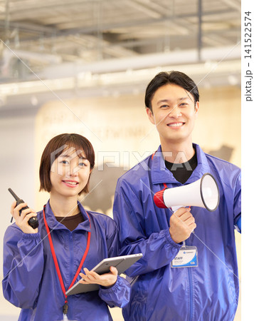 イベント会場でメガホンと無線機を手に笑顔を見せるスタッフの男女 141522574