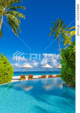 Tall palm trees over an infinity pool overlooking a turquoise tropical lagoon. White sand beach and blue sky at a luxury island resort. Summer vacation travel background. Tall palm trees over an infinity pool overlooking a turquoise tropical lagoon. White sand beach and blue sky at a luxury island resort. Summer vacation travel background. 141524866