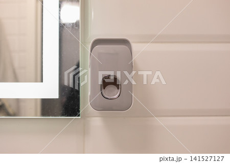 Wall-mounted automatic soap dispenser beside a bathroom mirror on white tiled wall, showing modern hygiene equipment, touchless hand washing, cleanliness and minimalist interiors Wall-mounted automatic soap dispenser beside a bathroom mirror on white tiled wall, showing modern hygiene equipment, touchless hand washing, cleanliness and minimalist interiors 141527127
