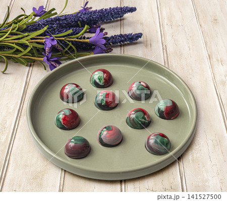 Collectible handmade tempered chocolate sweets with a glossy painted body on a round plate Collectible handmade tempered chocolate sweets with a glossy painted body on a round plate 141527500