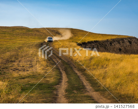Silver SUV driving on dirt road through golden hills Silver SUV driving on dirt road through golden hills 141527568
