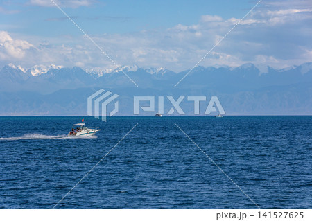 Speedboat with people on Issyk-Kul lake against snow-capped mountains in Kyrgyzstan Speedboat with people on Issyk-Kul lake against snow-capped mountains in Kyrgyzstan 141527625