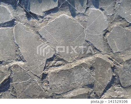 textured stone pavement made of uneven dark gray slabs. Large flat fragments are connected with cement mortar. The rough textured surface is covered with small cracks, chips and a grainy texture. textured stone pavement made of uneven dark gray slabs. Large flat fragments are connected with cement mortar. The rough textured surface is covered with small cracks, chips and a grainy texture. 141529106