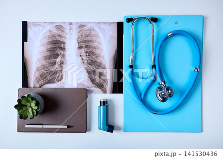Asthma treatment in medical clinic. Lung x-ray, medical documents and patient's inhaler on pulmonologists table during consultation, top view Asthma treatment in medical clinic. Lung x-ray, medical documents and patient's inhaler on pulmonologists table during consultation, top view 141530436
