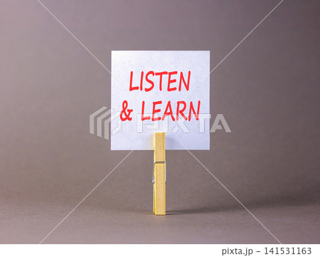 Listen and learn words symbol. Concept words Listen and learn on beautiful white paper on wooden clothespin. Beautiful grey background. Business listen and learn support concept. Copy space. 141531163