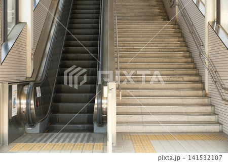 点字ブロックが敷かれた駅構内のエスカレーターと階段の構図。非常停止ボタンと安全警告ステッカー 点字ブロックが敷かれた駅構内のエスカレーターと階段の構図。非常停止ボタンと安全警告ステッカー 141532107