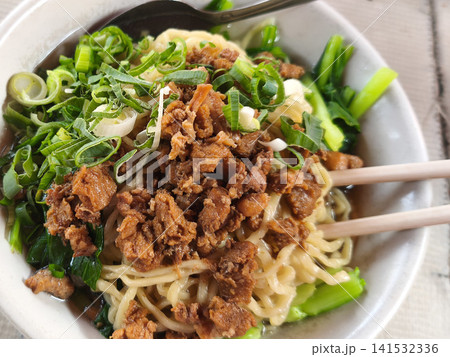 Indonesian chicken noodle bowl (Mie Ayam) topped with savory minced chicken, green vegetables, and scallions. Indonesian chicken noodle bowl (Mie Ayam) topped with savory minced chicken, green vegetables, and scallions. 141532336