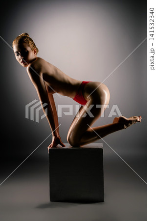 Woman posing on black cube in red underwear with dramatic studio lighting Woman posing on black cube in red underwear with dramatic studio lighting 141532340