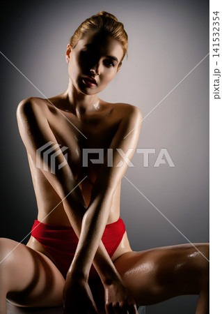 Woman in red bikini with glossy skin under dramatic studio lighting Woman in red bikini with glossy skin under dramatic studio lighting 141532354
